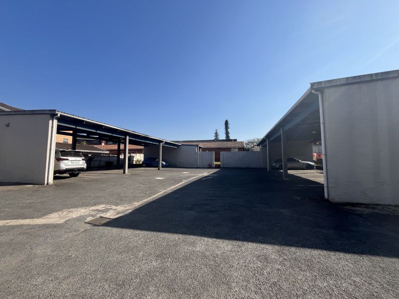 Open-air covered parking area with asphalt surfacing and structural support pillars for the flat complex.