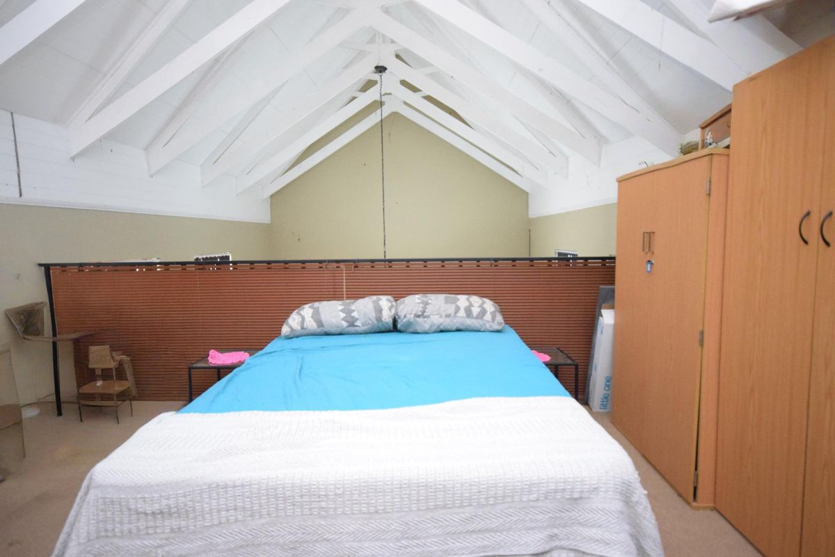 Spacious bedroom featuring a high vaulted ceiling with exposed white timber rafters and a mezzanine-style layout.