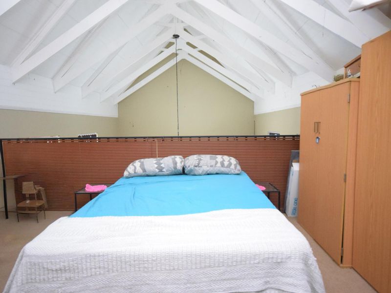 Spacious bedroom featuring a high vaulted ceiling with exposed white timber rafters and a mezzanine-style layout.