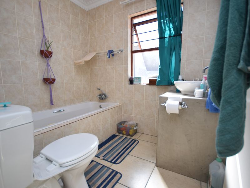 A functional bathroom featuring a bathtub, toilet, and a modern vessel sink set on a concrete-style vanity with neutral wall and floor tiling.