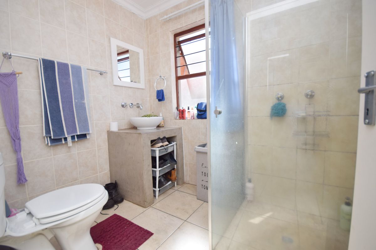 A functional bathroom featuring a concrete vanity with a vessel sink, a glass-enclosed shower, and neutral wall and floor tiling.