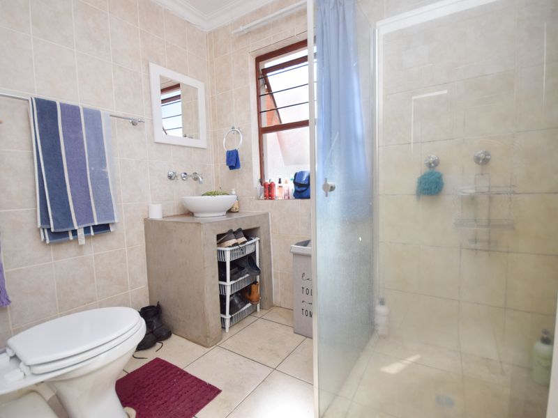 A functional bathroom featuring a concrete vanity with a vessel sink, a glass-enclosed shower, and neutral wall and floor tiling.