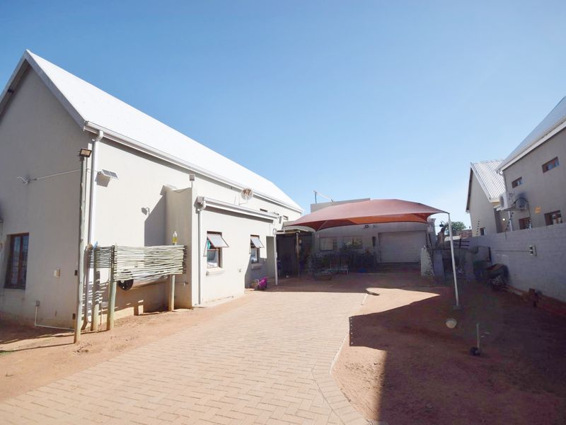 Rear exterior view featuring a paved driveway, a shade sail covering a parking area, and access to the garage.