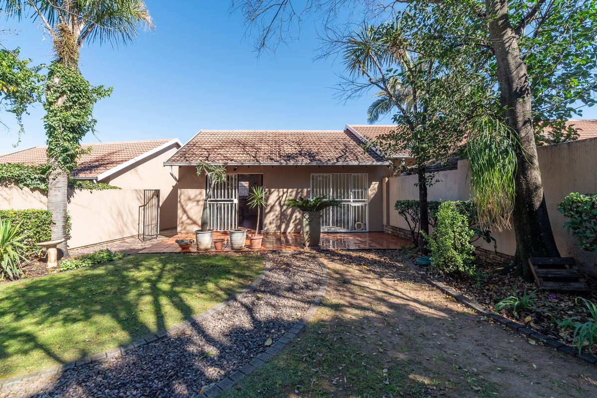 Rear view of the townhouse featuring a tiled patio, security gates, and a private garden with a gravel pathway and established trees.