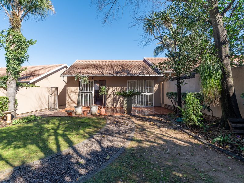 Rear view of the townhouse featuring a tiled patio, security gates, and a private garden with a gravel pathway and established trees.