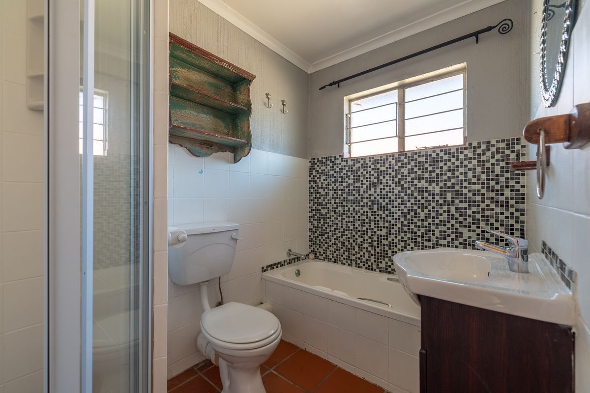 A functional bathroom featuring a shower enclosure, bathtub, vanity basin, and mosaic tile accents, offering a practical layout with potential for modern updates.