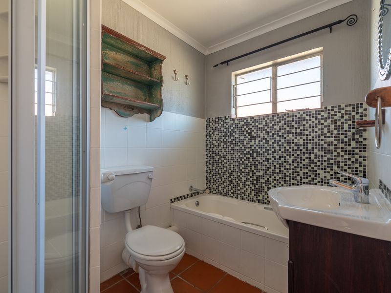 A functional bathroom featuring a shower enclosure, bathtub, vanity basin, and mosaic tile accents, offering a practical layout with potential for modern updates.