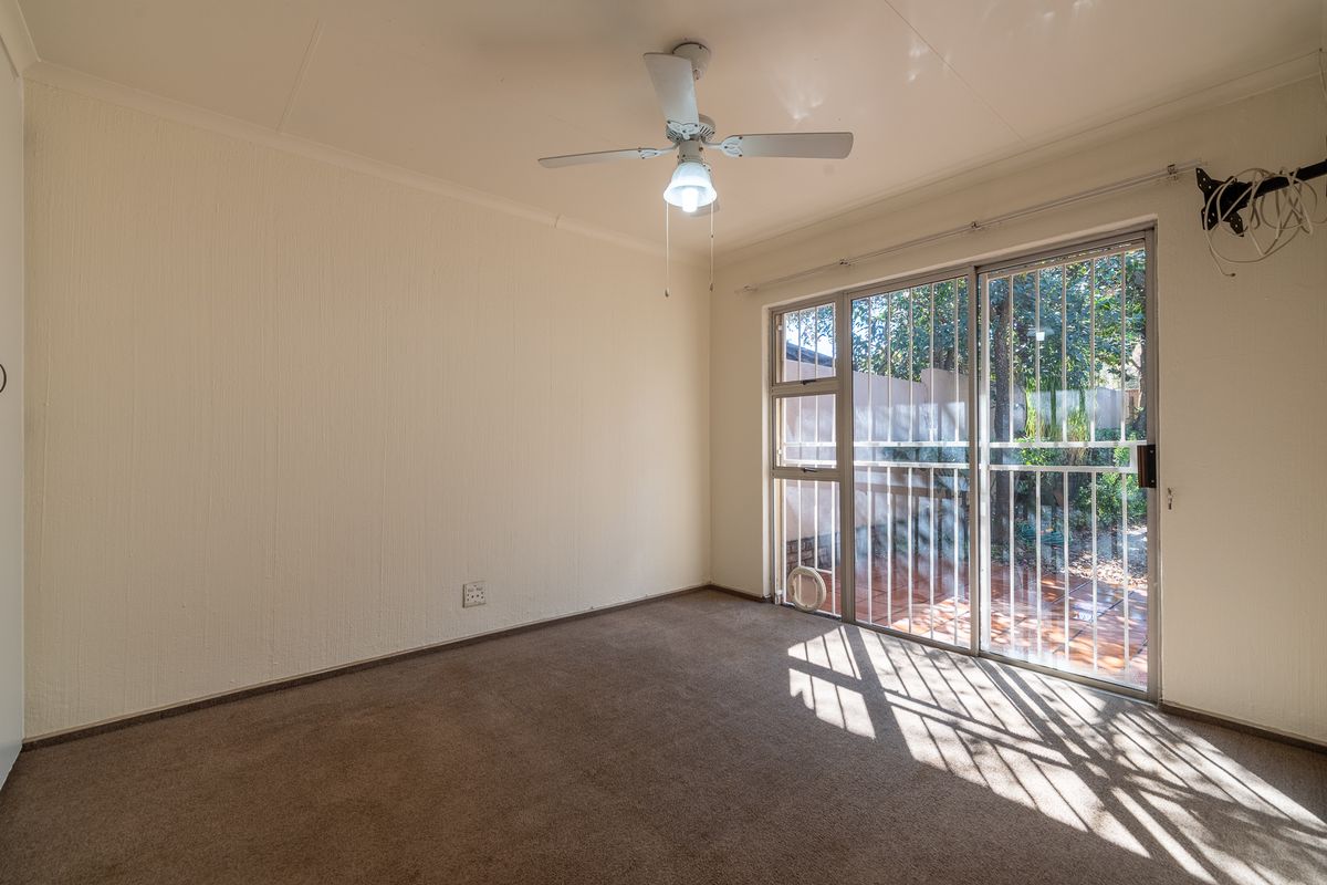 An empty bedroom featuring carpeted flooring, a ceiling fan, and a sliding glass door with security bars leading to an outdoor area.