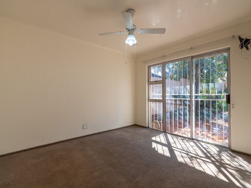 An empty bedroom featuring carpeted flooring, a ceiling fan, and a sliding glass door with security bars leading to an outdoor area.