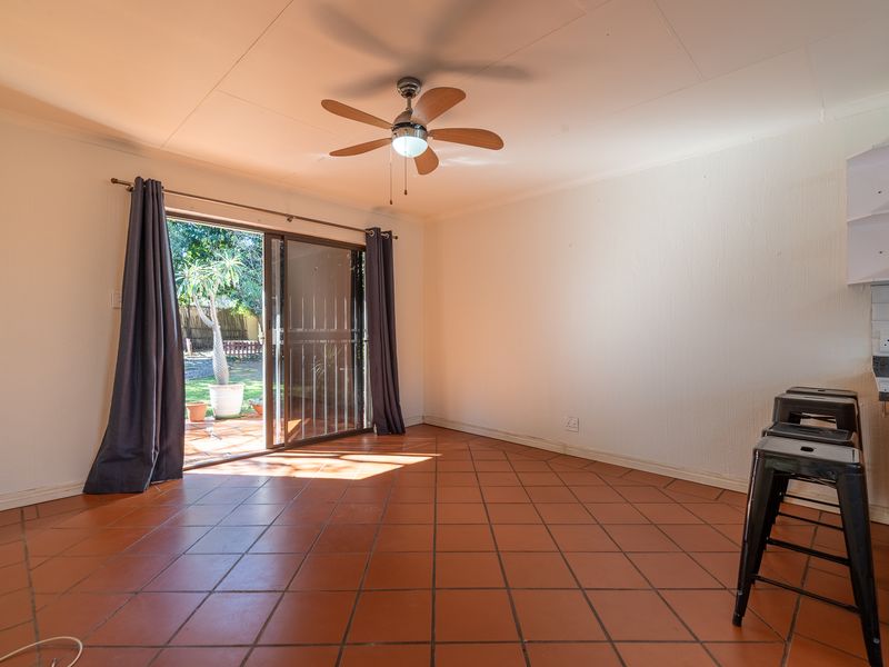 Open plan living area featuring terracotta tiled floors, a ceiling fan, and direct access to the rear garden through a sliding glass door.