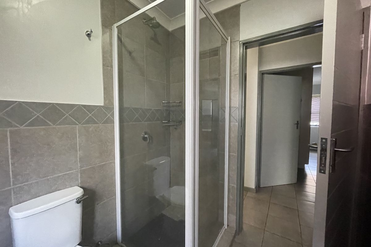 A functional bathroom featuring a glass shower enclosure, tiled walls, and a standard toilet, with direct access to the hallway.