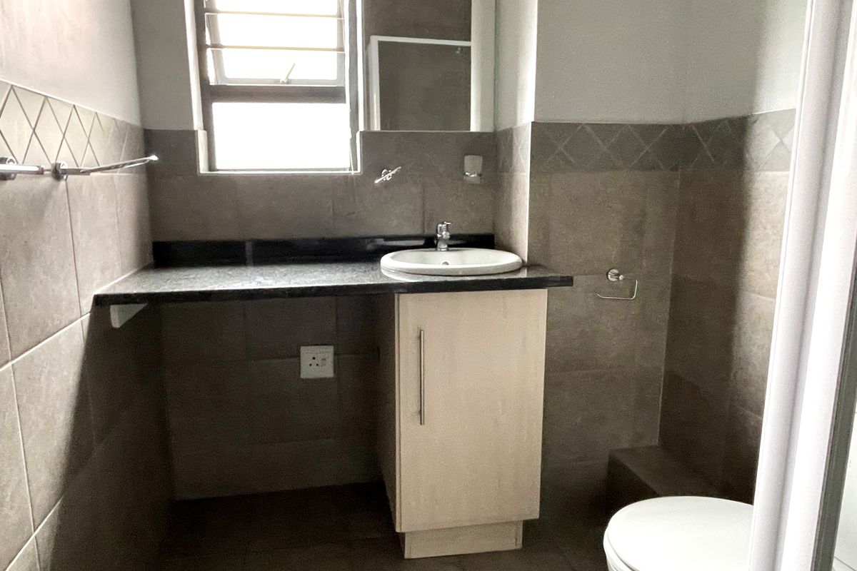 A functional bathroom featuring a vanity cabinet with a granite countertop, drop-in basin, and tiled finishes throughout.