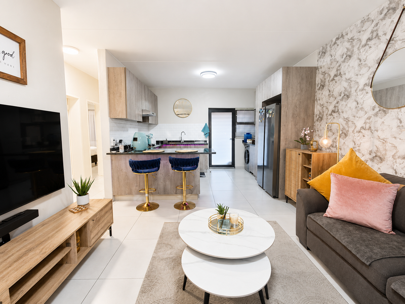 Modern open-plan living area featuring a contemporary kitchen with built-in cabinetry, a breakfast island, and sleek tiled flooring throughout the space.