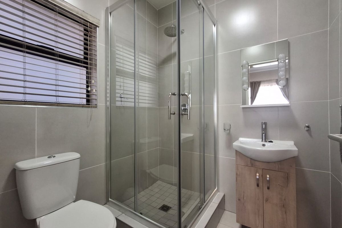 Modern bathroom featuring a glass-enclosed shower, contemporary vanity with basin, and neutral wall tiling throughout.