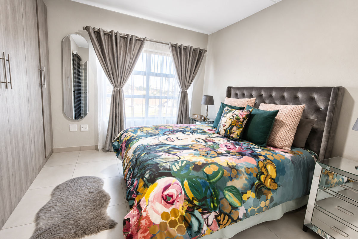 A well-maintained bedroom featuring neutral tiled flooring, built-in cupboards with wood-grain finish, and a large window allowing for natural light.