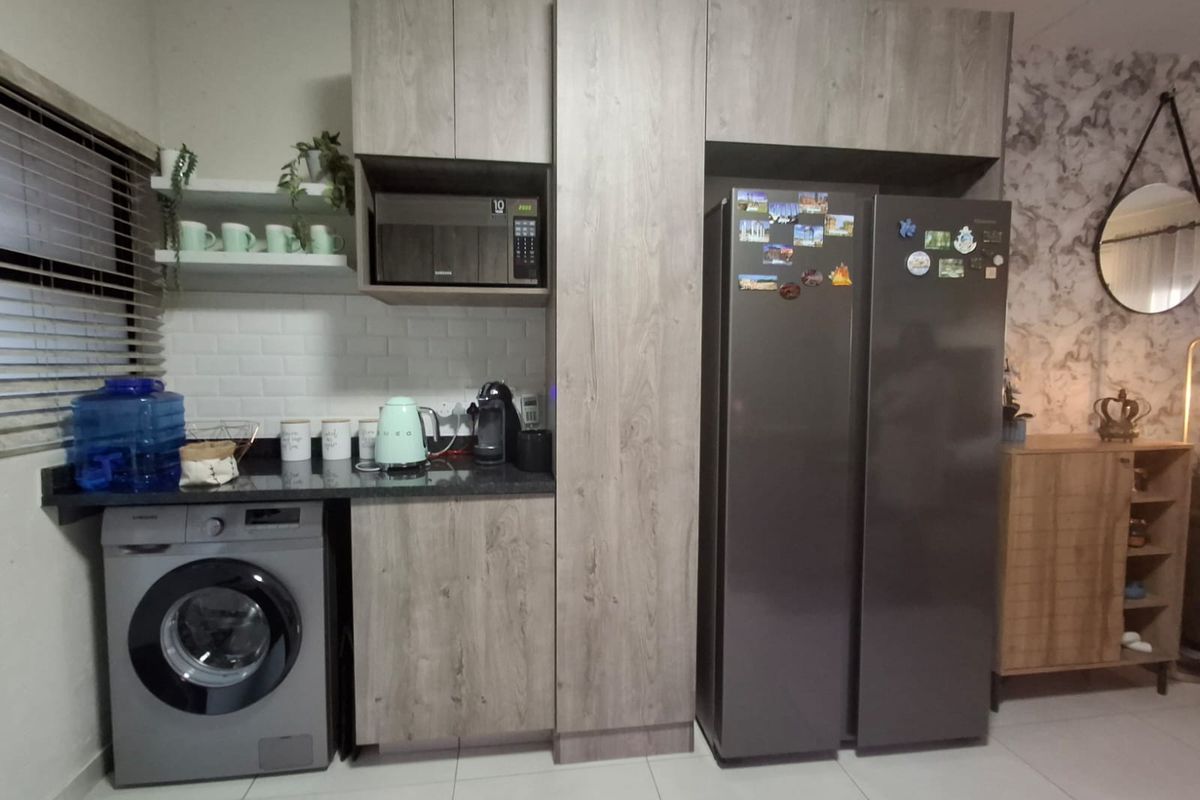 Modern kitchen area featuring wood-look cabinetry, stone countertops, subway tile backsplash, and integrated space for a washing machine and large refrigerator.