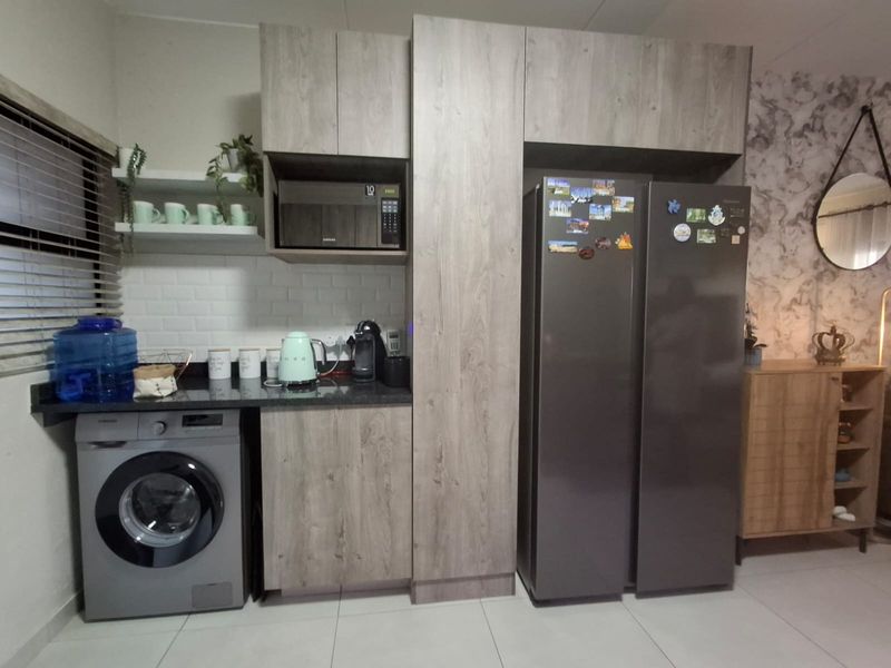 Modern kitchen area featuring wood-look cabinetry, stone countertops, subway tile backsplash, and integrated space for a washing machine and large refrigerator.