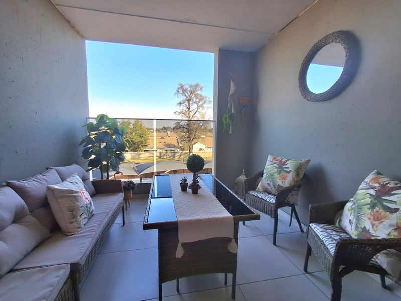 A covered balcony featuring tiled flooring and a modern glass balustrade, offering an open outdoor seating area.