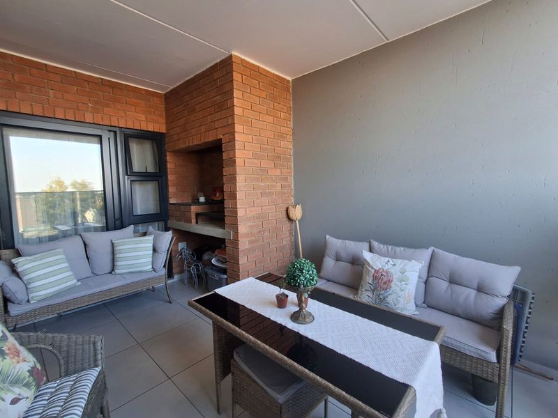 A covered balcony featuring tiled flooring and a built-in brick braai, providing a functional outdoor entertainment space.