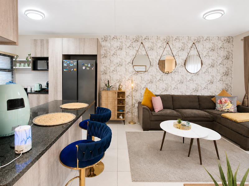 A modern open-plan living area featuring a well-appointed kitchen with stone countertops, subway tile backsplash, and a seamless transition into a comfortable lounge space.