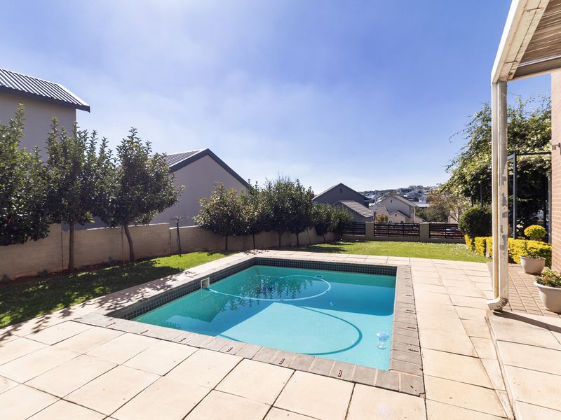 A private backyard featuring a swimming pool, paved patio area, and a covered outdoor space, set within a landscaped garden with boundary walls.