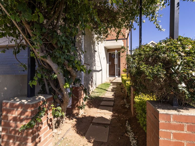 A front entrance pathway featuring brick pillars, a pergola structure, and established garden landscaping leading to the main building entrance.