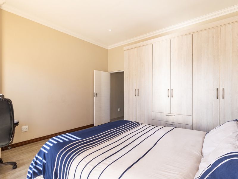 A well-maintained bedroom featuring light-toned built-in cupboards, laminate flooring, and decorative coving, providing a clean and functional living space.