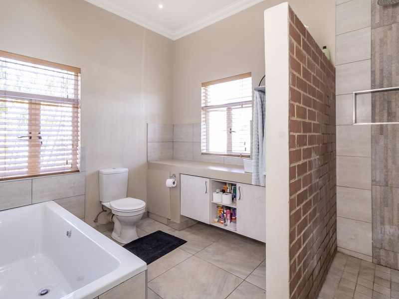 Spacious bathroom featuring a built-in vanity, bathtub, and a walk-in shower separated by an exposed brick partition wall.