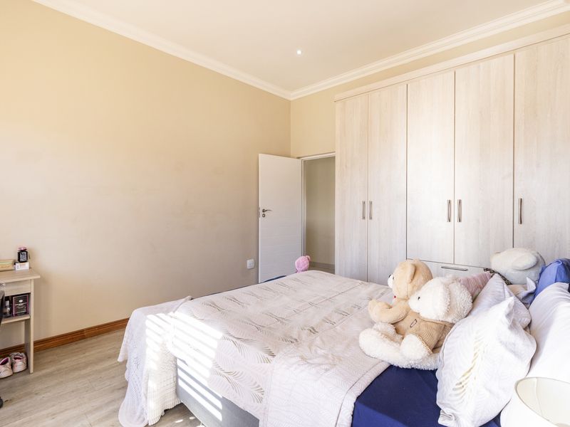 A well-maintained bedroom featuring light-toned laminate flooring, neutral wall finishes, and extensive built-in cupboard storage with modern hardware.