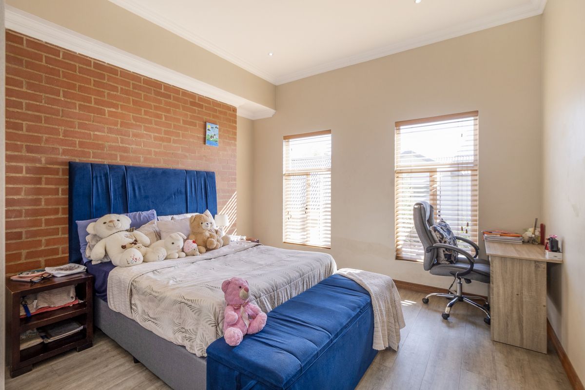 A well-lit bedroom featuring an exposed brick accent wall, laminate flooring, and dual windows with fitted venetian blinds.
