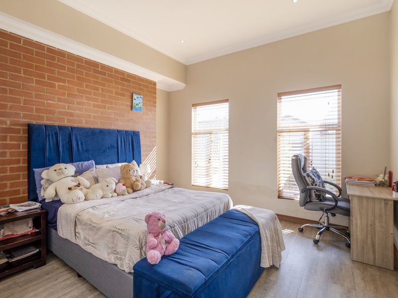 A well-lit bedroom featuring an exposed brick accent wall, laminate flooring, and dual windows with fitted venetian blinds.