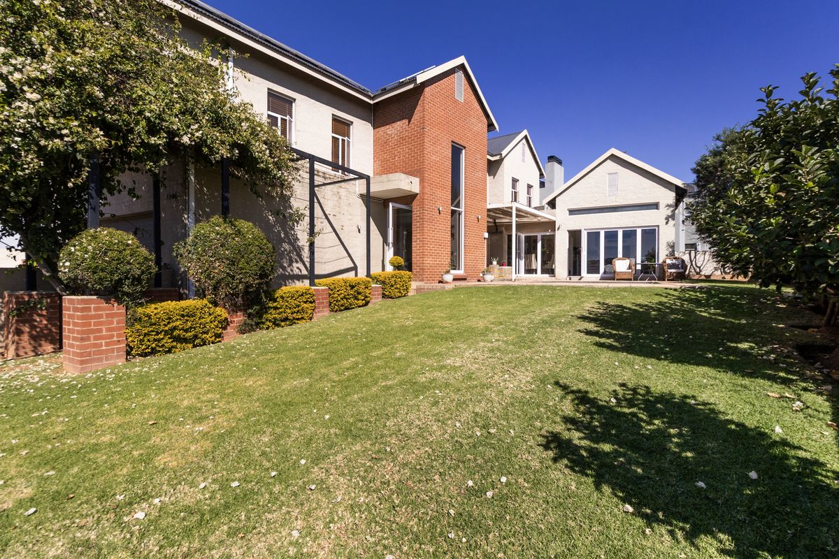 A well-maintained rear exterior view of the house featuring a spacious lawn, brick and plastered facade, and large sliding glass doors leading to the patio.