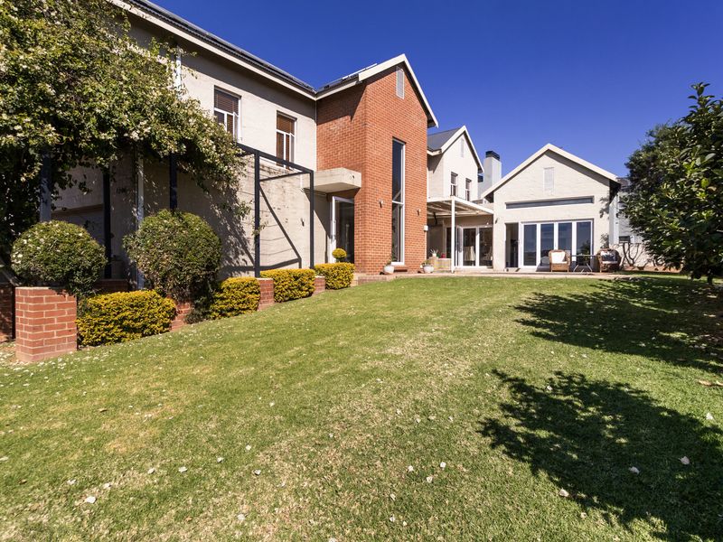 A well-maintained rear exterior view of the house featuring a spacious lawn, brick and plastered facade, and large sliding glass doors leading to the patio.