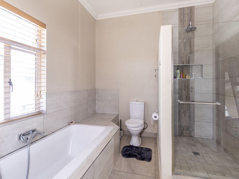 Modern bathroom featuring a built-in bathtub, a separate walk-in shower with tiled accents, and a toilet, finished with neutral wall and floor tiles.