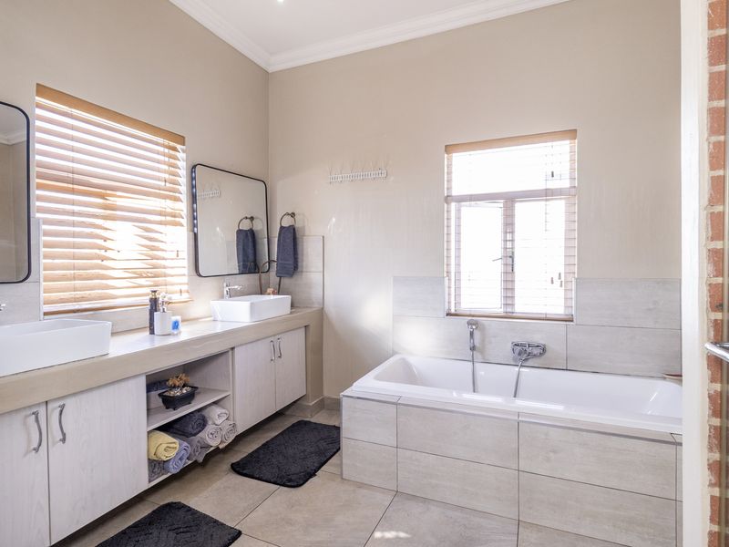Modern bathroom featuring a double vanity with vessel sinks, a tiled built-in bathtub, and neutral finishes with an exposed brick accent wall.