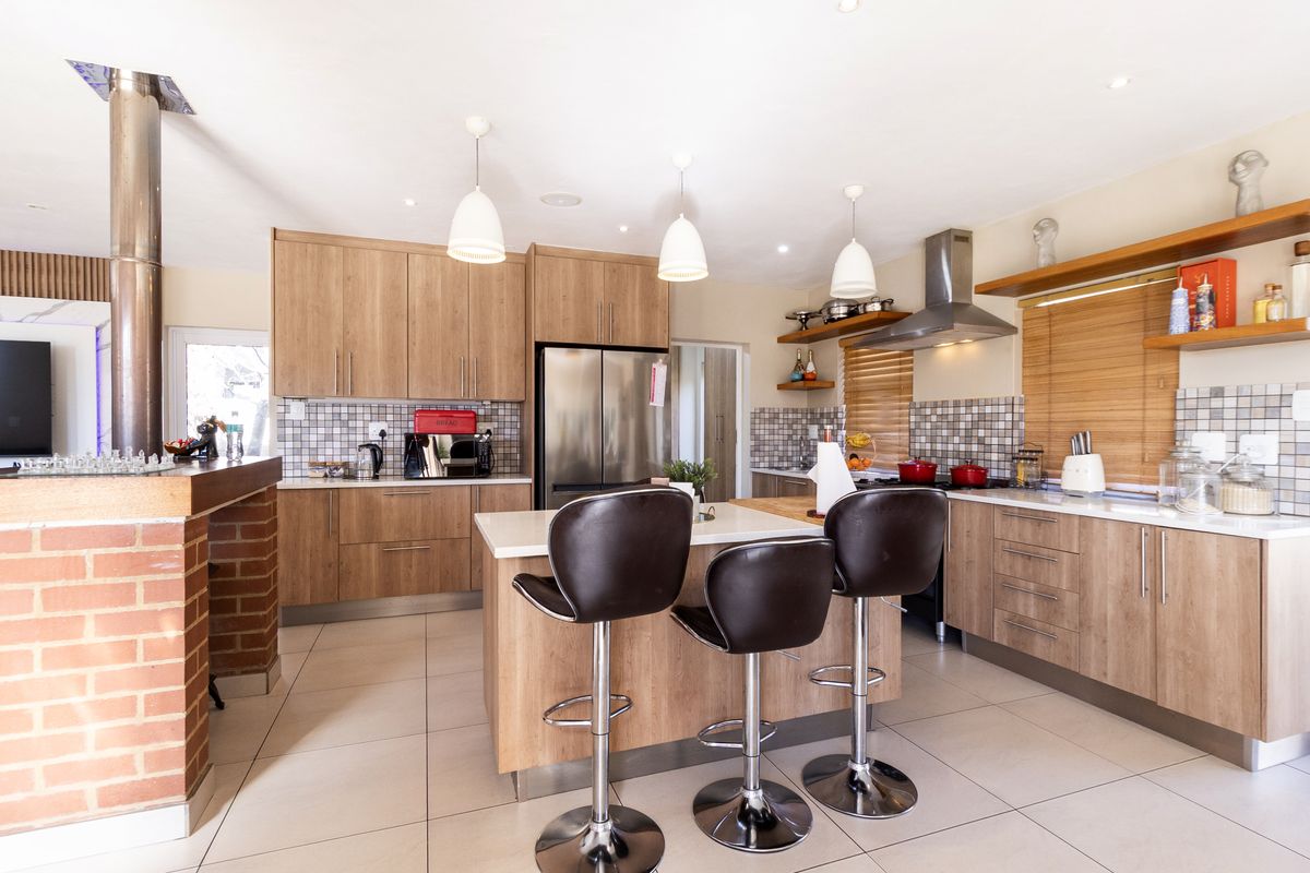 Modern kitchen featuring wood-finish cabinetry, a central island with breakfast seating, stainless steel appliances, and a distinctive brick-accented breakfast bar.