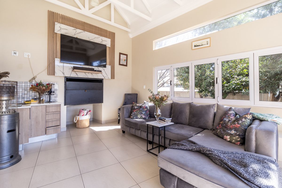 Bright living room featuring vaulted ceilings with exposed trusses, a modern fireplace with marble-look surround, timber slat accents, and large windows overlooking the garden.