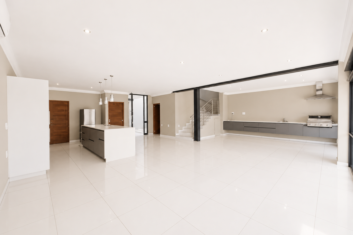 Spacious open-plan living and kitchen area featuring modern cabinetry, a central island, sleek tiled flooring, and a staircase leading to the upper level.