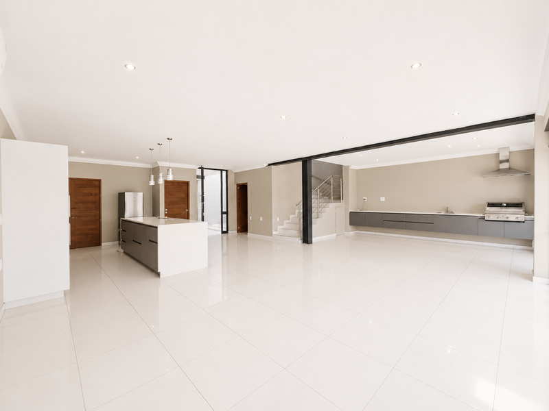 Spacious open-plan living and kitchen area featuring modern cabinetry, a central island, sleek tiled flooring, and a staircase leading to the upper level.