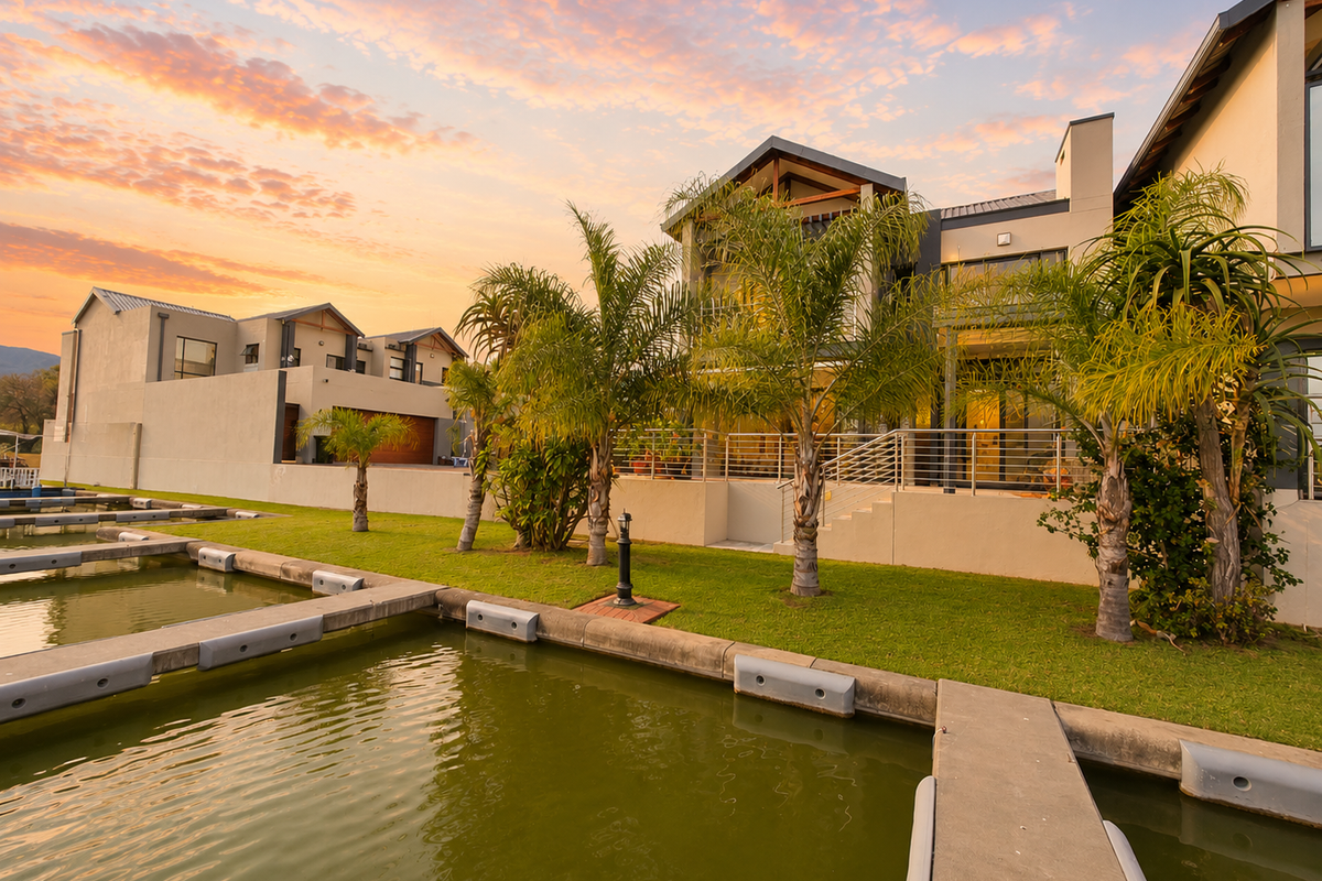 A stunning rear view of a modern waterfront property featuring a private boat jetty, manicured garden, and spacious patio overlooking the canal at sunset.