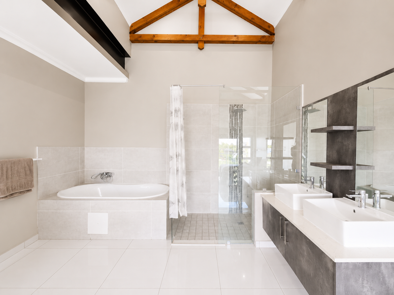 Modern bathroom featuring a built-in bathtub, walk-in shower, double vanity with stone countertop, and striking exposed timber roof trusses.