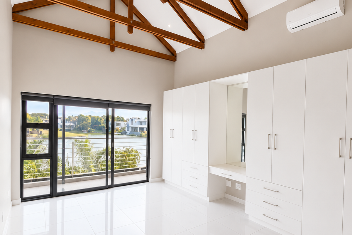 Spacious bedroom featuring high vaulted ceilings with exposed timber trusses, extensive built-in cabinetry with vanity, tiled flooring, and sliding doors opening to a balcony.