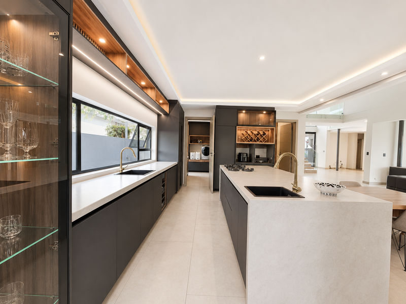 Modern, high-end kitchen featuring a large stone island, sleek dark cabinetry, integrated wine storage, brass fixtures, and premium recessed lighting.