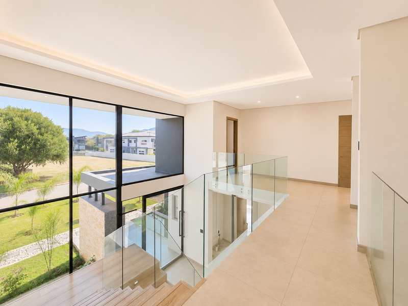 Spacious modern landing area featuring a glass balustrade, large format floor tiles, recessed ceiling lighting, and expansive windows overlooking the garden.