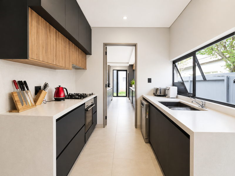 Modern galley-style kitchen featuring sleek matte black and wood-grain cabinetry, stone countertops, integrated appliances, and a gas hob with a clean, contemporary finish.