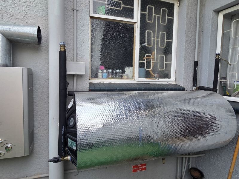 Exterior wall featuring a gas geyser and an insulated hot water cylinder with security burglar bars on the windows.
