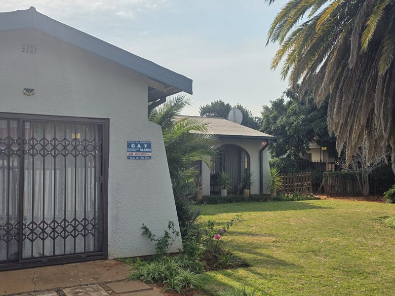 A view of the rear exterior of the property featuring a plastered facade, security gate, and a well-maintained garden area.