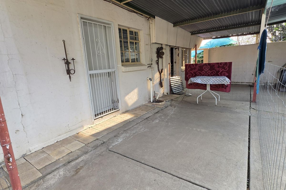 A covered outdoor patio area featuring a concrete floor and corrugated metal roofing, providing a functional space for outdoor utility or relaxation.