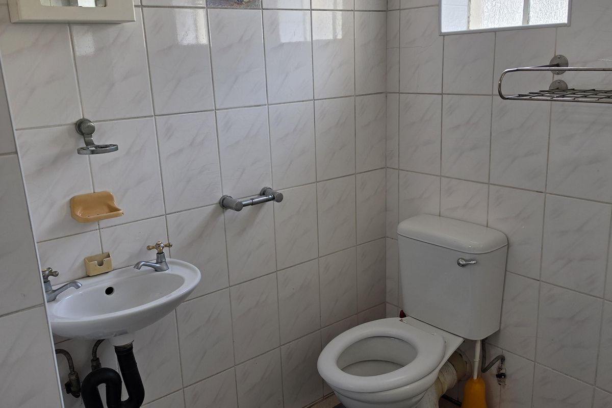 A compact bathroom featuring a wall-mounted basin, toilet, and fully tiled walls. The space is functional but would benefit from modern updates.