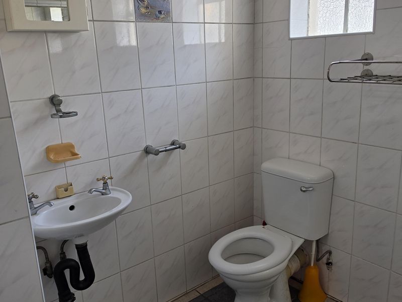 A compact bathroom featuring a wall-mounted basin, toilet, and fully tiled walls. The space is functional but would benefit from modern updates.